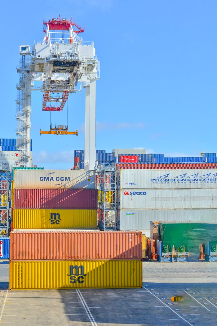 about-us Stacked cargo containers in a sunny port industrial setting with crane.